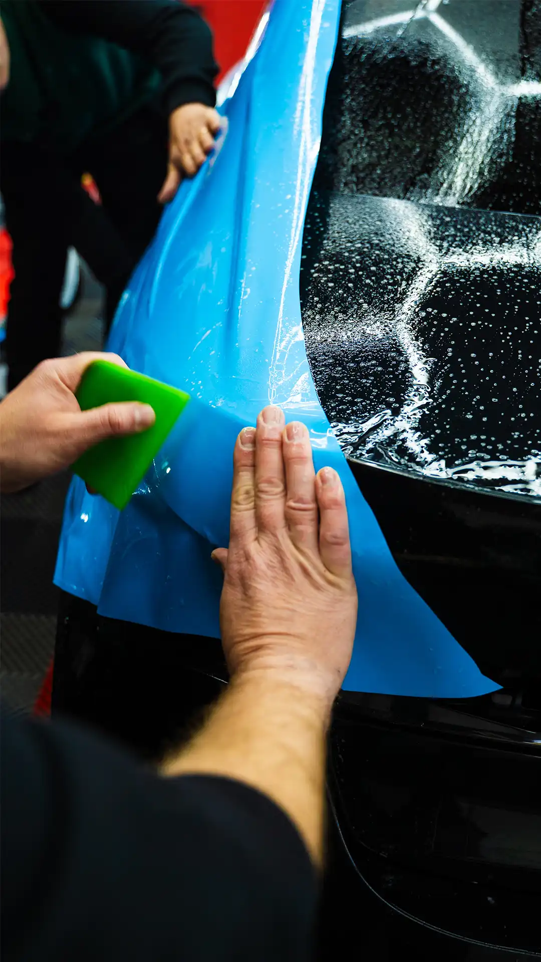 Clear paint protection film being smoothed onto a blue vehicle panel